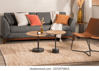 Mid-Century Modern Living Room with Gray Upholstered Sofa, Decorative Throw Pillows, Warm Beige Blanket, Round Wood Side Table, Decorative Glass Bottle Vases, Leather Lounge Accent Chair, Area Rug.