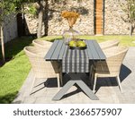 Mid-Century Modern Rectangular Patio Dining Set with Rattan Chairs in Sunny Home Garden, Adorned with Table Runner, Vase of Flowers, and Fresh Fruits for Breakfast.