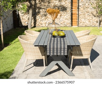 Mid-Century Modern Rectangular Patio Dining Set with Rattan Chairs in Sunny Home Garden, Adorned with Table Runner, Vase of Flowers, and Fresh Fruits for Breakfast. - Powered by Shutterstock