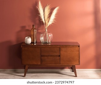 Mid-Century Modern Wooden Sideboard with Glass Vase Decoration Set with Pampas grass, Against a Salmon-Colored Wall in the Interior of a Living Room with Wooden Flooring.