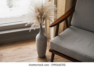 Mid-century retro chair and pampas grass bouquet in clay pot against window with curtains. Modern aesthetic minimalist home, living room interior design concept