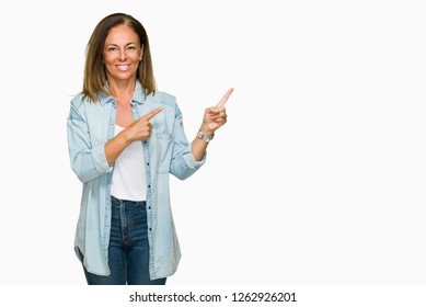 Middle age adult woman wearing casual denim shirt over isolated background with a big smile on face, pointing with hand and finger to the side looking at the camera. - Shutterstock ID 1262926201