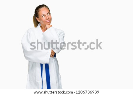 Middle age adult woman wearing karate kimono uniform over isolated background with hand on chin thinking about question, pensive expression. Smiling with thoughtful face. Doubt concept.