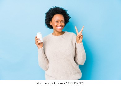 Middle age african american woman holding a vitamin bottle showing number two with fingers.