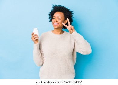 Middle age african american woman holding a vitamin bottle showing victory sign and smiling broadly.