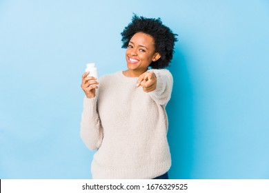 Middle age african american woman holding a vitamin bottle cheerful smiles pointing to front.
