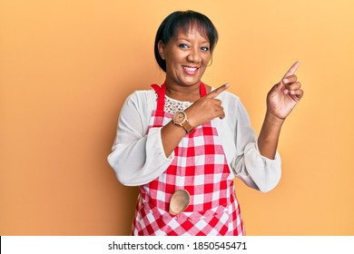 Middle age african american woman wearing baker uniform smiling and looking at the camera pointing with two hands and fingers to the side. 