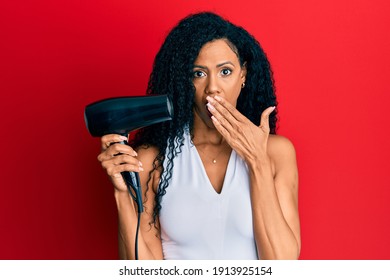 Middle Age African American Woman Holding Hair Dryer Covering Mouth With Hand, Shocked And Afraid For Mistake. Surprised Expression 