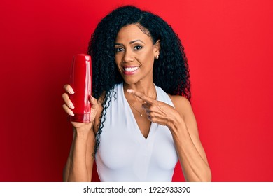 Middle Age African American Woman Holding Shampoo Bottle Smiling Happy Pointing With Hand And Finger 