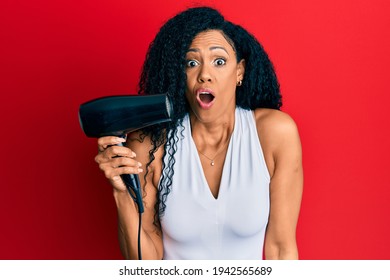 Middle Age African American Woman Holding Hair Dryer Scared And Amazed With Open Mouth For Surprise, Disbelief Face 