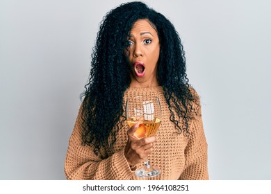 Middle age african american woman drinking a glass of white wine scared and amazed with open mouth for surprise, disbelief face 