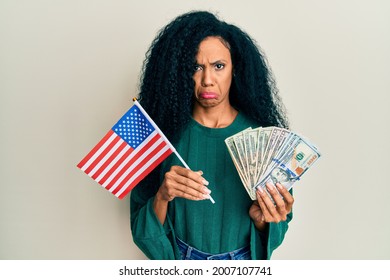 Middle Age African American Woman Holding United States Flag And Dollars Depressed And Worry For Distress, Crying Angry And Afraid. Sad Expression. 