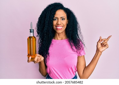 Middle Age African American Woman Holding Olive Oil Can Smiling Happy Pointing With Hand And Finger To The Side 