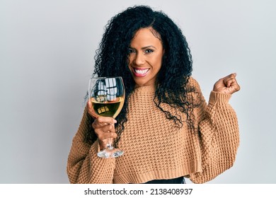 Middle Age African American Woman Drinking A Glass Of White Wine Screaming Proud, Celebrating Victory And Success Very Excited With Raised Arm 