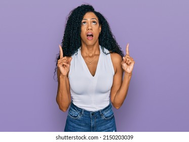 Middle Age African American Woman Wearing Casual Style With Sleeveless Shirt Amazed And Surprised Looking Up And Pointing With Fingers And Raised Arms. 