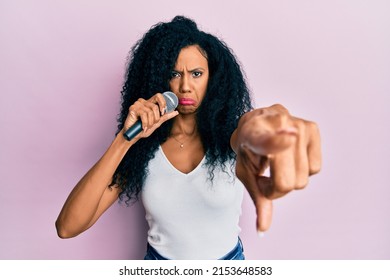 Middle Age African American Woman Singing Song Using Microphone Pointing With Finger Depressed And Worry For Distress, Crying Angry And Afraid. Sad Expression. 