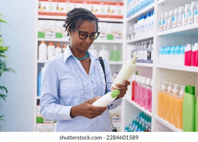 Middle age african american woman customer holding shampoo bottles at pharmacy - Powered by Shutterstock