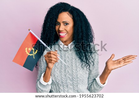 Middle age african american woman holding angola flag celebrating achievement with happy smile and winner expression with raised hand 
