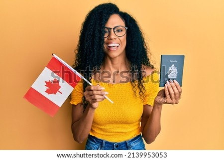 Middle age african american woman holding canada flag and passport smiling and laughing hard out loud because funny crazy joke. 