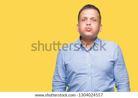 Middle age arab business man over isolated background puffing cheeks with funny face. Mouth inflated with air, crazy expression.