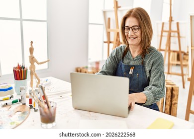 Middle age artist woman smiling happy using laptop at art studio.