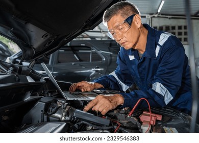 Middle age Asian car mechanic man using his computer to check the engine while working on the car in his garage shop - Powered by Shutterstock