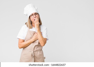 middle age baker woman yawning lazily early in the morning, waking and looking sleepy, tired and bored against flat wall