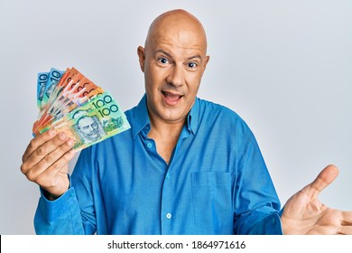 Middle age bald man holding australian dollars celebrating achievement with happy smile and winner expression with raised hand 