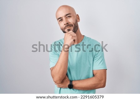 Middle age bald man standing over white background looking confident at the camera smiling with crossed arms and hand raised on chin. thinking positive. 