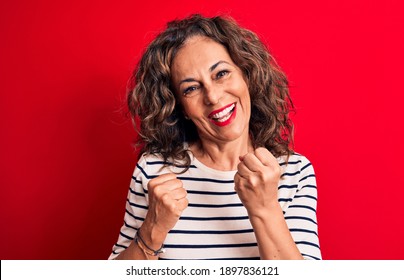 Middle age beautiful brunette woman wearing striped t-shirt standing over red background celebrating surprised and amazed for success with arms raised and eyes closed