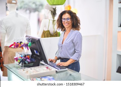 Middle age beautiful clothes shop owner woman smiling happy and confident working with computer at counter - Powered by Shutterstock