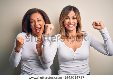 Middle age beautiful couple of sisters wearing casual t-shirt over isolated white background celebrating surprised and amazed for success with arms raised and open eyes. Winner concept.