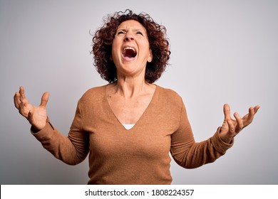 Middle age beautiful curly hair woman wearing casual sweater over isolated white background crazy and mad shouting and yelling with aggressive expression and arms raised. Frustration concept.