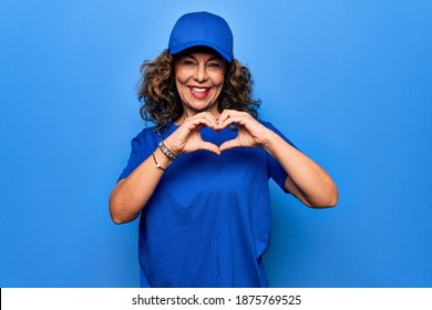 Middle age beautiful delivery woman wearing blue uniform and cap over isolated background smiling in love doing heart symbol shape with hands. Romantic concept.