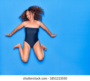 Middle Age Beautiful Hispanic Woman On Vacation Wearing Swimsuit Smiling Happy. Jumping With Smile On Face Over Isolated Blue Background