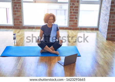 Middle age beautiful sportswoman smilig happy. Sitting on mat with smile on face using laptop at home