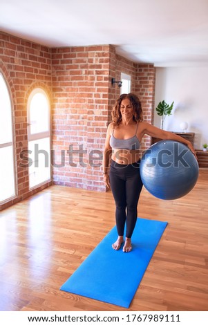 Middle age beautiful sportswoman smiling happy. Doing exercise using fitness ball in a class of yoga at gym