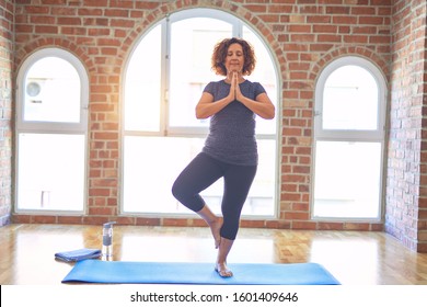 Middle age beautiful sportwoman smiling happy. Standing on mat practicing yoga doing tree pose at gym