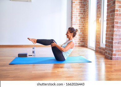 Middle Age Beautiful Sportwoman Smiling Happy. Sitting On Mat Practicing Yoga Doing Boat Pose At Gym