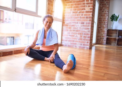 Middle age beautiful sportwoman smiling happy and confident. Sitting on the floor with smile on face after doing exercise at gym