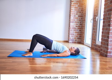 Middle age beautiful sportwoman smiling happy. Lying down on mat practicing yoga doing bridge pose at gym