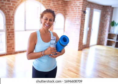 Middle Age Beautiful Sportwoman Smiling Happy And Confident. Standing With Smile On Face Holding Mat And Bottle Of Water Before Doing Exercise At Gym