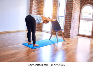 Middle age beautiful sportwoman standing on mat. Practicing yoga doing down dog on chair pose at gym