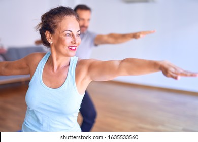 Middle Age Beautiful Sporty Couple Smiling Happy. Standing With Smile On Face Practicing Yoga Doing Warrior Pose At Gym