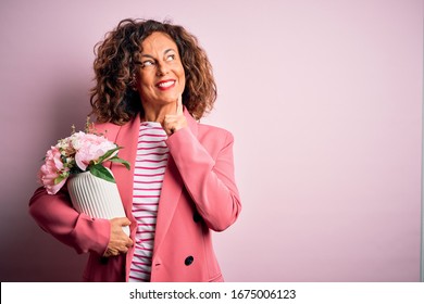 Middle Age Beautiful Woman Holding Vase With Flowers Over Isolated Pink Background Serious Face Thinking About Question, Very Confused Idea