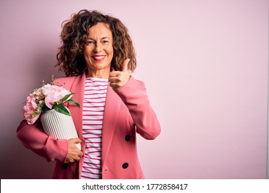 Middle Age Beautiful Woman Holding Vase With Flowers Over Isolated Pink Background Happy With Big Smile Doing Ok Sign, Thumb Up With Fingers, Excellent Sign