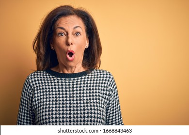 Middle age beautiful woman wearing casual sweater over isolated yellow background afraid and shocked with surprise expression, fear and excited face.