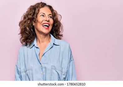Middle Age Beautiful Woman Wearing Casual Denim Shirt Standing Over Pink Background Looking Away To Side With Smile On Face, Natural Expression. Laughing Confident.