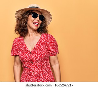 Middle age beautiful woman wearing casual dress and sunglasses over yellow background looking to side, relax profile pose with natural face and confident smile.