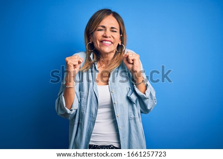 Middle age beautiful woman wearing casual shirt standing over isolated blue background excited for success with arms raised and eyes closed celebrating victory smiling. Winner concept.